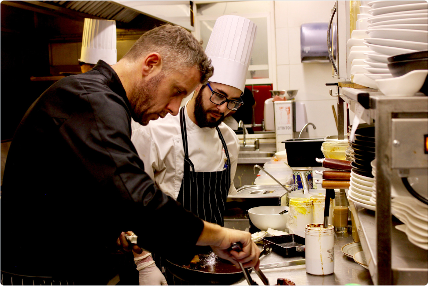 Team of chefs plating gourmet meal together in upscale kitchen